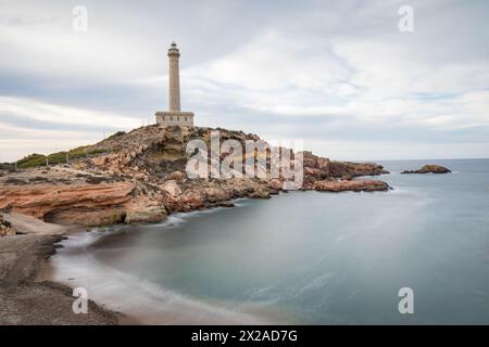 Vista a lunga esposizione del faro di Cabo de Palos sulla costa rocciosa di Cartagena, regione di Murcia, Spagna, che si affaccia sul tranquillo Mar Mediterraneo. Foto Stock