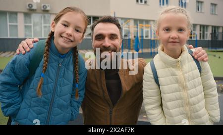 Felice uomo di famiglia due ragazze papà figlie scolaresche studenti scuola elementare insieme amore genitore sorridente coccole abbraccio studenti compagni di classe Foto Stock