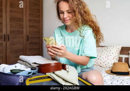 Prenotazione online di un hotel e acquisto di biglietti elettronici di volo tramite smartphone. La donna si prepara a viaggiare. Foto Stock