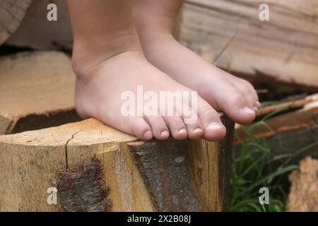 Piedi per bambini su tronco di legno, bambina a piedi nudi su tronco d'albero, stile di vita rurale, concetto di messa a terra e collegamento con la natura Foto Stock