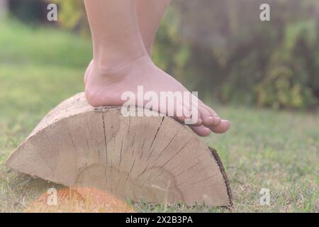 Piedi per bambini su tronco di legno, bambina a piedi nudi su tronco d'albero, stile di vita rurale, concetto di messa a terra e collegamento con la natura Foto Stock