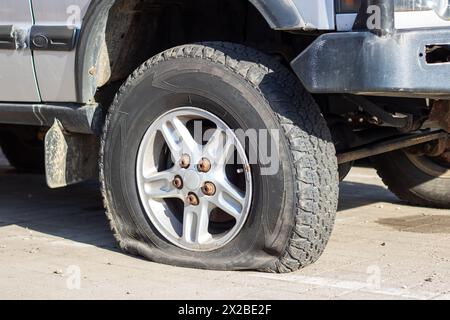 Un'auto con uno pneumatico per auto sgonfio sul lato della strada, che mostra la ruota in lega e i mozzi di bloccaggio. Il battistrada in gomma sintetica è visibile, wi Foto Stock