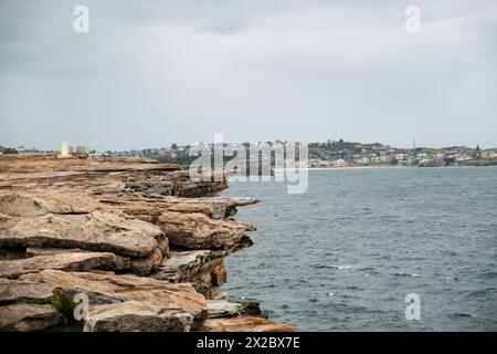 Passeggiata costiera da Bondi a Coogee in una giornata nuvolosa, con aspre pietre che costeggiano il sentiero sulla sinistra e la vasta distesa del mare che si estende Foto Stock