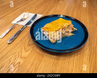 Un pezzo di casseruola di patate con funghi e pollo ricoperto da crosta di formaggio sul piatto blu scuro Foto Stock