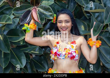 Una ballerina sorridente Hula Hawaii in piedi accanto a un ficus elastica - albero di gomma. Foto Stock