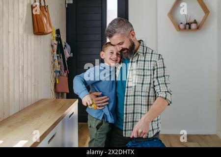 Padre che aiuta figlio a prepararsi per l'asilo, asilo. Pantalone, scarpe, cestino per il pranzo con spuntini. Foto Stock