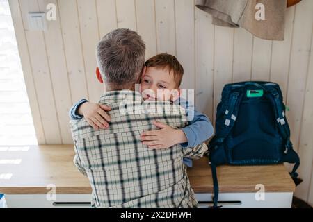 Padre che aiuta figlio a prepararsi per l'asilo, asilo. Abbracciare, abbracciare. Pantalone, scarpe, cestino per il pranzo con spuntini. Foto Stock