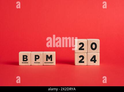 L'abbreviazione BPM Business Process Management dell'anno 2024 su cubi di legno con sfondo rosso. Foto Stock