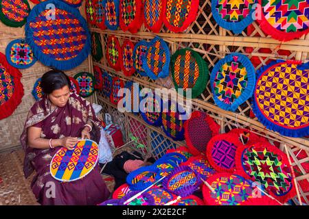 Narayanganj, Dacca, Bangladesh. 22 aprile 2024, Narayanganj, Dacca, Bangladesh: I lavoratori ricamano sapientemente ventilatori a mano con forme geometriche dai colori vivaci a Narayanganj, Bangladesh. Utilizzano bambù e filati colorati per creare ventilatori dal design complesso. Durante le estati calde, danno una brezza fresca che aiuta quando fa davvero caldo all'aperto in caso di distacco del carico. Ogni lavoratore può contare su 10 tifosi al giorno, ogni fan viene venduto per circa 1,20 USD alle fiere dei villaggi. Questa è diventata una professione tradizionale nella zona, fanno fan a mano da centinaia di anni. Credito: ZUMA Press, in Foto Stock