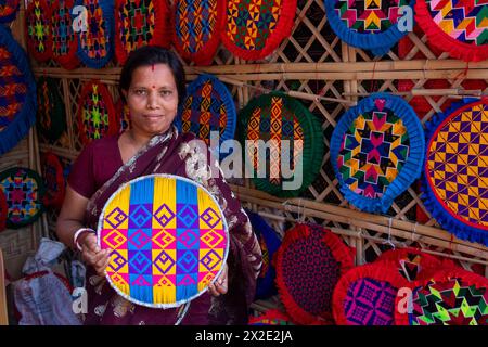 Narayanganj, Dacca, Bangladesh. 22 aprile 2024, Narayanganj, Dacca, Bangladesh: I lavoratori ricamano sapientemente ventilatori a mano con forme geometriche dai colori vivaci a Narayanganj, Bangladesh. Utilizzano bambù e filati colorati per creare ventilatori dal design complesso. Durante le estati calde, danno una brezza fresca che aiuta quando fa davvero caldo all'aperto in caso di distacco del carico. Ogni lavoratore può contare su 10 tifosi al giorno, ogni fan viene venduto per circa 1,20 USD alle fiere dei villaggi. Questa è diventata una professione tradizionale nella zona, fanno fan a mano da centinaia di anni. Credito: ZUMA Press, in Foto Stock