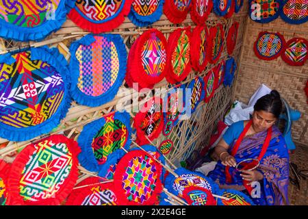 Narayanganj, Dacca, Bangladesh. 22 aprile 2024, Narayanganj, Dacca, Bangladesh: I lavoratori ricamano sapientemente ventilatori a mano con forme geometriche dai colori vivaci a Narayanganj, Bangladesh. Utilizzano bambù e filati colorati per creare ventilatori dal design complesso. Durante le estati calde, danno una brezza fresca che aiuta quando fa davvero caldo all'aperto in caso di distacco del carico. Ogni lavoratore può contare su 10 tifosi al giorno, ogni fan viene venduto per circa 1,20 USD alle fiere dei villaggi. Questa è diventata una professione tradizionale nella zona, fanno fan a mano da centinaia di anni. Credito: ZUMA Press, in Foto Stock