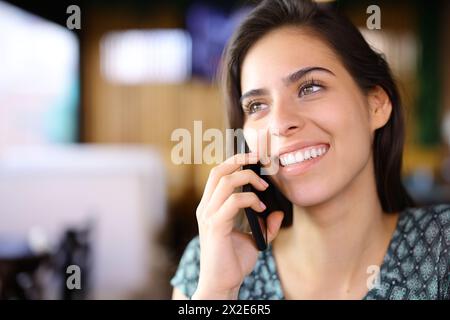 Donna felice in un bar che parla al telefono con un sorriso perfetto Foto Stock