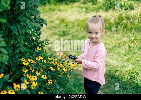 Un bambino esamina un fiore sotto una lente d'ingrandimento Foto Stock