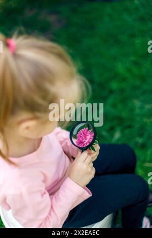 Un bambino esamina un fiore sotto una lente d'ingrandimento Foto Stock