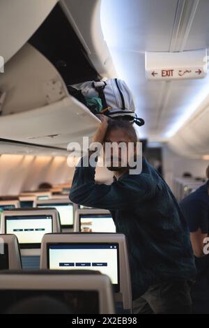 L'uomo su un aereo mette i suoi bagagli sullo scaffale. Foto Stock