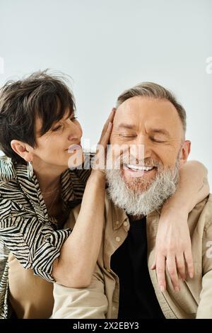 Un uomo e una donna di mezza età in un abbigliamento elegante si siedono a stretto contatto, trasudando un senso di connessione e compagnia. Foto Stock