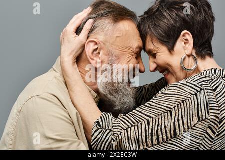 Un uomo e una donna di mezza età in un abbigliamento elegante che si abbracciano intimamente in un ambiente da studio. Foto Stock