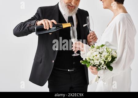 Sposo e sposa di mezza età, vestito con abiti da sposa, regala con gioia champagne in un ambiente da studio. Foto Stock