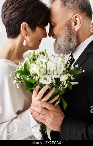 Sposa di mezza età e sposo in abito da sposa, con un bellissimo bouquet di fiori, per celebrare il loro giorno speciale in un ambiente studio. Foto Stock