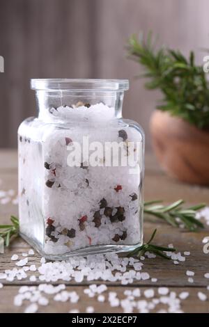 Sale con grani di pepe in vaso di vetro e rosmarino su un tavolo di legno Foto Stock