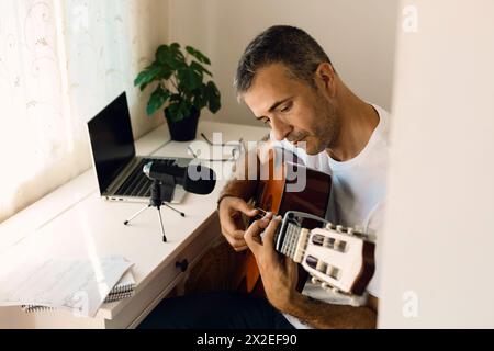 Uomo di mezza età che registra il suono della sua chitarra mentre si pratica a casa. Stile di vita concettuale Foto Stock