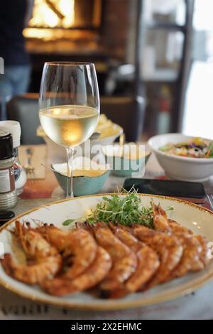 Langoustine con salsa di spinaci su un piatto bianco su un tavolo di marmo con un bicchiere di vino bianco. Foto di alta qualità Foto Stock