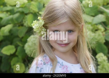 Ritratto all'aperto di una bambina felice con un fiore verde dietro l'orecchio Foto Stock