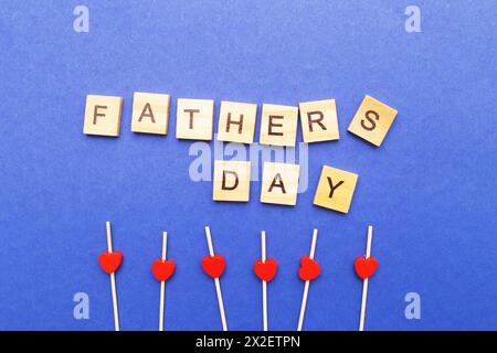 La parola del giorno del Padre fatta da cubetti di legno. Biglietto di auguri per il padre. Cuori rossi su sfondo blu. Foto Stock