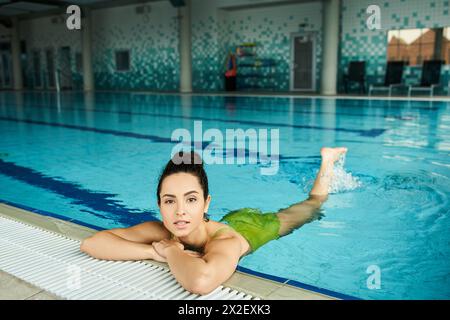 Una giovane, bella donna bruna in un costume da bagno verde si rilassa in una piscina all'interno di un ambiente spa interno. Foto Stock