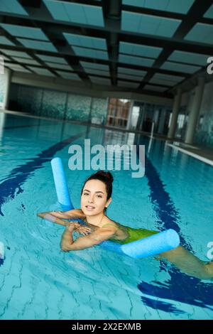 Una giovane donna in una piscina, che tiene con grazia un salvagente, trasuda calma e sicurezza in un ambiente spa interno. Foto Stock