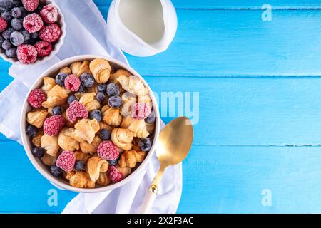 Minuscoli croissant a colazione, cereali con frutti di bosco freschi e latte. Ciotola con piccoli croissant alla moda appena sfornati con lampone e blueber Foto Stock