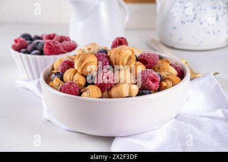 Minuscoli croissant a colazione, cereali con frutti di bosco freschi e latte. Ciotola con piccoli croissant alla moda appena sfornati con lampone e blueber Foto Stock