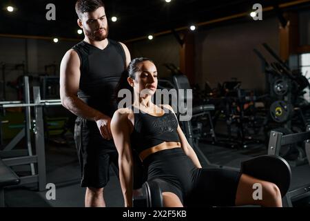 Un allenatore maschile si trova accanto a una donna sportiva bruna in palestra, aiutandola con una routine di allenamento. Foto Stock