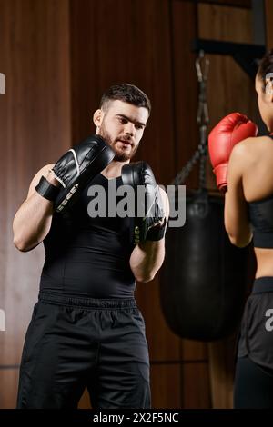 Un allenatore maschile che indossa guanti da boxe si trova accanto a una donna sportiva bruna indossata durante una sessione di boxe in una palestra. Foto Stock