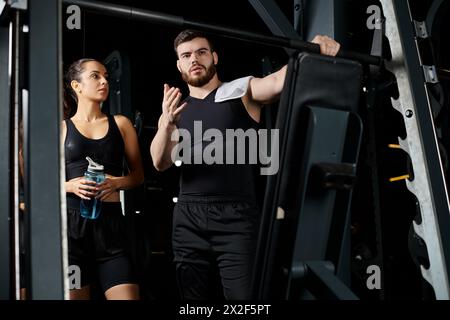 Un personal trainer maschile si trova accanto a una sportiva bruna in palestra, motivandola e guidandola durante una sessione di allenamento. Foto Stock