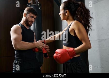 Un allenatore maschile si trova accanto a una sportiva bruna indossando guanti da boxe e praticando in palestra. Foto Stock