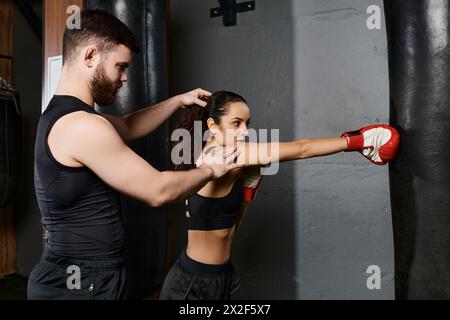 Un allenatore maschile sta accanto a una donna sportiva bruna in abbigliamento attivo, entrambi impegnati nel pugilato in palestra. Foto Stock