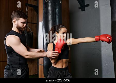 Un allenatore maschile si trova vicino a una sportiva bruna mentre si impegnano in una sessione di boxe in una palestra. Foto Stock