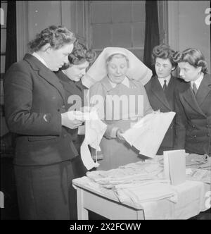 WRENS LEARN MOTHERCRAFT: I MEMBRI DEL WOMEN'S ROYAL NAVAL SERVICE RICEVONO UNA FORMAZIONE DALLA SOCIETÀ DI FORMAZIONE MOTHERCRAFT, LONDRA, INGHILTERRA, Regno Unito, 1945 - la Matron Miss Maslen-Jones mostra abiti per bambini a un gruppo di Wrens come parte della formazione che ricevono dalla Mothercraft Training Society, probabilmente alla sede centrale della MTS a Highgate, Londra. Secondo la didascalia originale, questi vestiti sono stati fatti da infermieri tirocinanti. "Questi indumenti sono progettati per un'economia dei materiali, ma con la dovuta considerazione per la salute e il benessere" Foto Stock