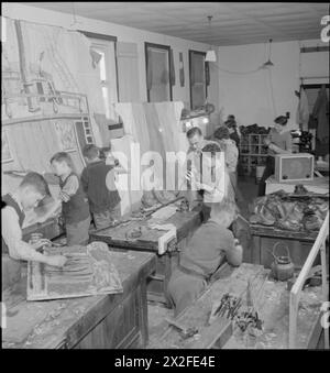 IMPARARE DALLA RECITAZIONE: EDUCAZIONE ATTRAVERSO IL TEATRO PER GLI SFOLLATI IN Una "SCUOLA DI CAMPO", MARCHANT'S HILL, HINDHEAD, SURREY, 1943 - il signor Fry (centro) supervisiona i ragazzi più grandi come stivali di riparazione nell'officina della Marchant's Hill School. In primo piano, gli altri ragazzi dipingono scenari, creano spade che usciranno dai loro pugnali e costruiscono alberi e lati delle navi per il gioco. Tutti nella scuola stanno contribuendo alla performance in qualche modo o in altro Foto Stock