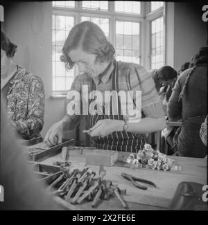 COMBATTONO ANCHE QUELLI CHE SI LIMITANO AD ASPETTARE: LAVORO DI GUERRA PART-TIME A CROYDON, SURREY, INGHILTERRA, 1943 - la signora Duncan lavora sull'assemblaggio di gambe a compressione in quella che era una volta la sala da pranzo di questa casa a Shirley, Croydon, ora utilizzata come officina. La signora Duncan è una casalinga e lavora in questa "fabbrica” da quando è stata aperta a febbraio Foto Stock