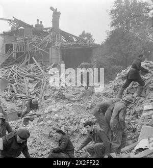 BOMBA VOLANTE: DANNI DA BOMBA V1 A LONDRA, INGHILTERRA, Regno Unito, 1944 - i soccorritori della difesa civile cercano tra pile di macerie mentre cercano di scacciare i sopravvissuti fuori dagli edifici crollati a seguito di un attacco V1 nella zona di Highland Road e Lunham Road a Norwood, Londra, SE19. Uno sta usando un cane per aiutare nella ricerca. Sullo sfondo, una casa mezzo distrutta può essere chiaramente vista Foto Stock