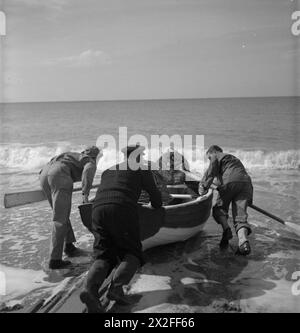 TRUPPE STATUNITENSI IN UN VILLAGGIO INGLESE: VITA QUOTIDIANA CON GLI AMERICANI A BURTON BRADSTOCK, DORSET, INGHILTERRA, Regno Unito, 1944 - PFC George W Burnett (a sinistra, della Route 5, Spartanburg, South Carolina) e PFC Harris L Whitwell (a sinistra, di Main Street, Rogersville, Tennessee) aiutano il pescatore locale Tom Swaffield a lanciare la sua barca a remi al sole del Dorset. Tom sta portando il GIS fuori per vedere le sue pentole di aragosta Foto Stock