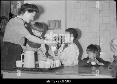 HOPSCOTCH INN: IL LAVORO DEL SAVE THE CHILDREN FUND IN TEMPO DI GUERRA LONDRA, INGHILTERRA, Regno Unito, 1944 - il Club Warden Kathleen Fox consegna una tazza di cacao e un rotolo a George Megan (del 10 St Augustine's House, London, NW1) al Save the Children club in Eversholt Street, Euston. George ha un padre e uno zio nell'esercito. Potrai inoltre gustare i rinfreschi Carmel e Teresa (nascosta dal suo George) Parascandalo (del 122 Eversholt Street) e un altro giovane ragazzo sulla destra. La famiglia Parascandalo ha vissuto a Malta per tutta la guerra Foto Stock