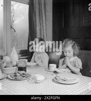 LUSSEMBURGHESI IN INGHILTERRA: SFOLLATI NEL SURREY, 1942 - Andrew di cinque anni e sua sorella Jacqueline di tre anni dicono Grace prima di un pasto nella casa in cui alloggiano nel Surrey. Secondo la didascalia originale, quando si siedono a mangiare "ricordano sempre i nonni ancora in Lussemburgo, il cibo è scarso in Lussemburgo ora” Foto Stock