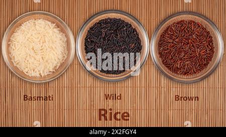 Tre ciotole trasparenti mostrano diverse varietà di riso: Basmati, Wild e Brown. L'assortimento rappresenta diversi tipi di cereali utilizzati in cu internazionale Foto Stock