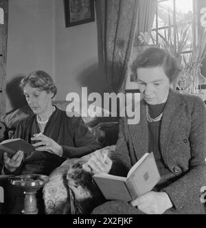 LA SIGNORA BUGLER VA IN GUERRA: EVERYDAY LIFE IN EAST DEAN, SUSSEX, INGHILTERRA, 1943 - la signora Macdonald (a sinistra) e la signorina Clements si godono un libro come parte del Reading Circle, che si tiene nella casa della signora Bugler a East Dean, Sussex Foto Stock