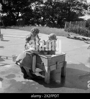 SCUOLA MATERNA MODELLO: IL LAVORO DELLA SCUOLA MATERNA TERRESTRE TARNER, BRIGHTON, SUSSEX, INGHILTERRA, REGNO UNITO, 1944 - le ragazze giocano nell'acqua attraverso il sole nel parco giochi della Tarner Land Nursery School Foto Stock