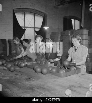 STICKY BOMB: THE PRODUCTION OF THE No 74 GRANADE IN BRITAIN, 1943 - Miss A Blackshow (centro, con occhiali) guarda come quattro operaie di guerra impacchettano bombe adesive in gruppi di cinque in piccole casse per il trasporto in una fabbrica di riempimento per l'aggiunta di esplosivi. La signorina Blackshow e' la capostipite responsabile dell'officina Foto Stock