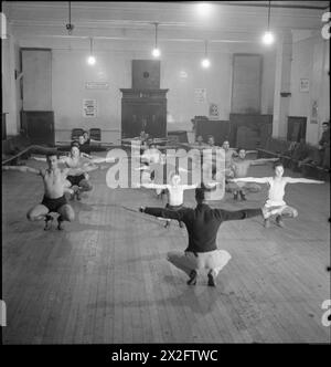 LONDON JEWS IN WARTIME: THE WORK OF YOUTH CLUBS IN STEPNEY, LONDON, 1942 - Una classe PT in corso nel ginnasio del Bernhard Baron Settlement Boys' club, Berner Street, Commercial Road. Lo sport e l'esercizio fisico erano estremamente importanti nell'educazione di questi ragazzi all'insediamento. I manifesti sul muro della palestra indicano che c'è il PT e la boxe ogni martedì e giovedì, e la Croce Rossa pronto soccorso e formazione infermieristica domiciliare lunedì e giovedì. Un altro poster recita: "Allenati subito per addestrare gli altri dopo - unisciti al corpo dei cadetti" Foto Stock